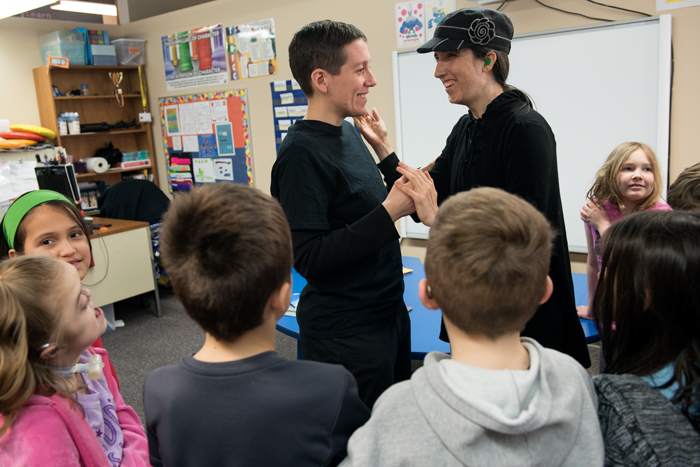 Teacher Wendy Harris greets an adult volunteer while surrounded by 2nd and 3rd grade students