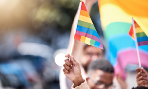 Young Black people carry LGBTQ flags in what looks like a parade. 