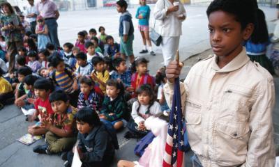 African American Student holding the US flag while younger students are sitting on the floor