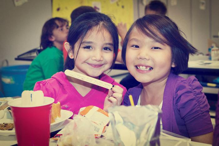 Two girls smiling while sharing lunch at cafeteria