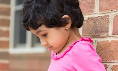 girl standing against brick wall looking down