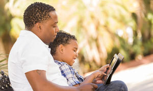 father and son looking at ipad outdoors