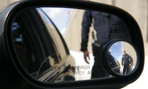 Police officer seen approaching in a car's side mirror.