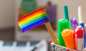 Small LGBTQ flag sitting in bin with writing utensils.
