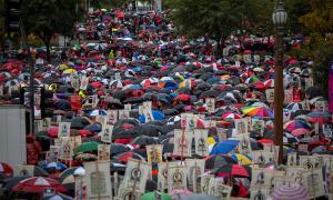 Hundreds of people gathered together, holding protest signs and umbrellas in Los Angeles, California.