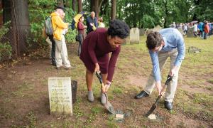 Two young people with spades digging near a burial marker.