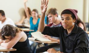 Young African-American teenager raising their hand in class.