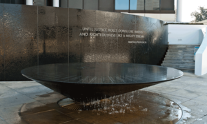 Photograph of the Civil Rights Memorial wall and fountain. The words "...until justice rolls down like waters and righteousness like a mighty stream. —Martin Luther King Jr." appear plainly on the wall.