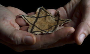 Two hands holding a faded cloth Star of David symbol.
