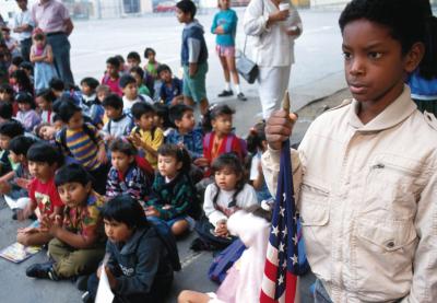 African American Student holding the US flag while younger students are sitting on the floor