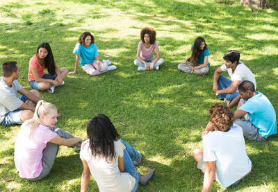 Young people sit in a circle on the grass.