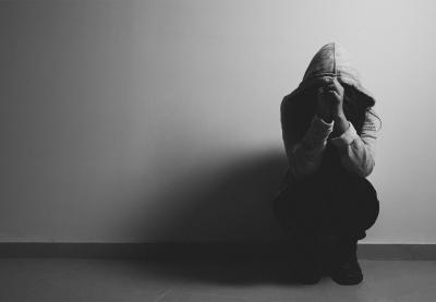 Distraught student sitting against wall with hoodie drawn