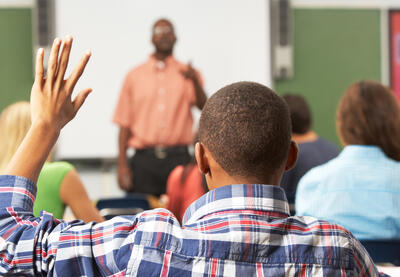 African-American student raising their hand in class, seen from behind.