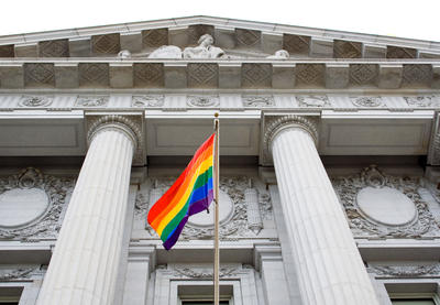 LGBTQ pride flag flying in front of courthouse-like building.