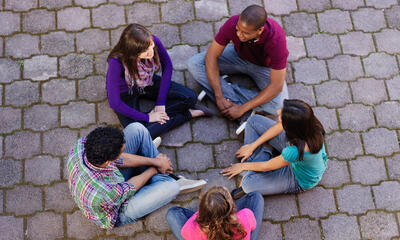 A group of teens sits in a circle having a conversation. 