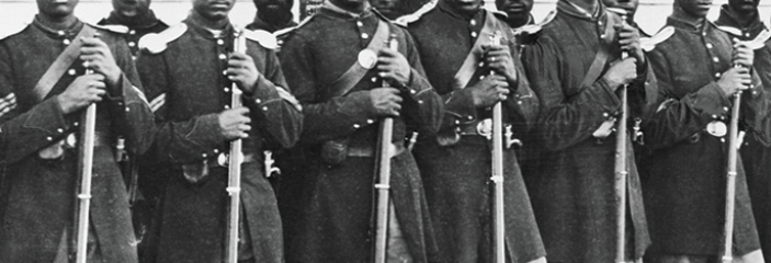 Black Union soldiers standing outside in a line in uniform looking at the camera