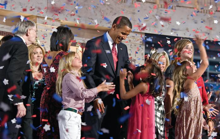 Barak Obama surrounded by children under a confetti rain