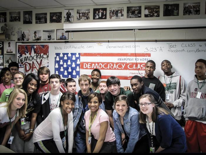 Students participating in Rock the Vote pose in front of American flag