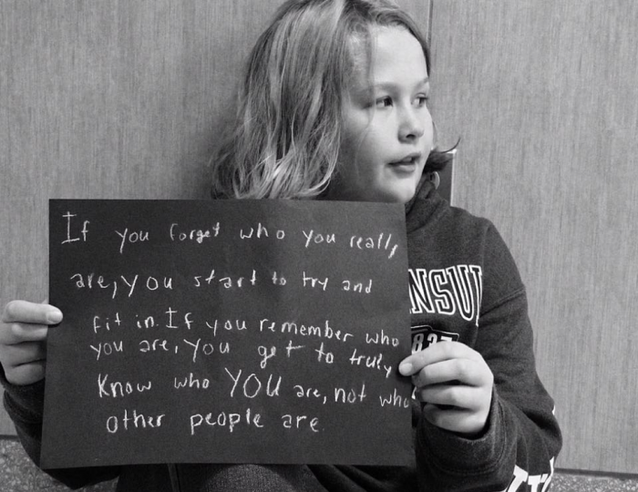Young student holding a sign that says "If you forget who you really are, you start to try and fit in. If you remember who you are, you get to truly know who YOU are, not who other people are."