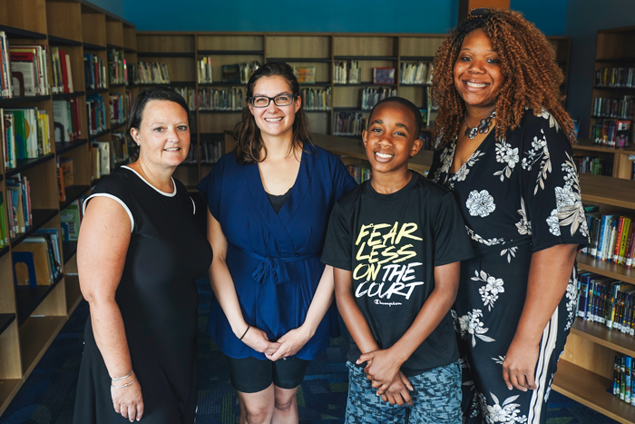 Kaylan Lelito, librarian Jennifer Chapman, Dontae White and Leah White standing together between shelves filled with books in a library.
